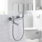 Ducha higiênica Royal Concept cromada instalada em banheiro branco claro ao lado do vaso sanitário