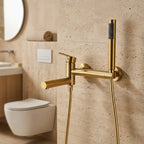 Ducha higiênica Royal Concept dourado escovado instalada em parede de travertino em banheiro sofisticado