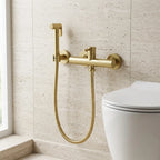 Ducha higiênica Royal Neo dourado escovado instalada em parede de travertino ao lado do vaso sanitário