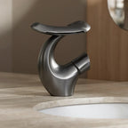 Torneira Lumiere Cinza instalada em bancada de pedra clara, com bica curva e comando circular lateral