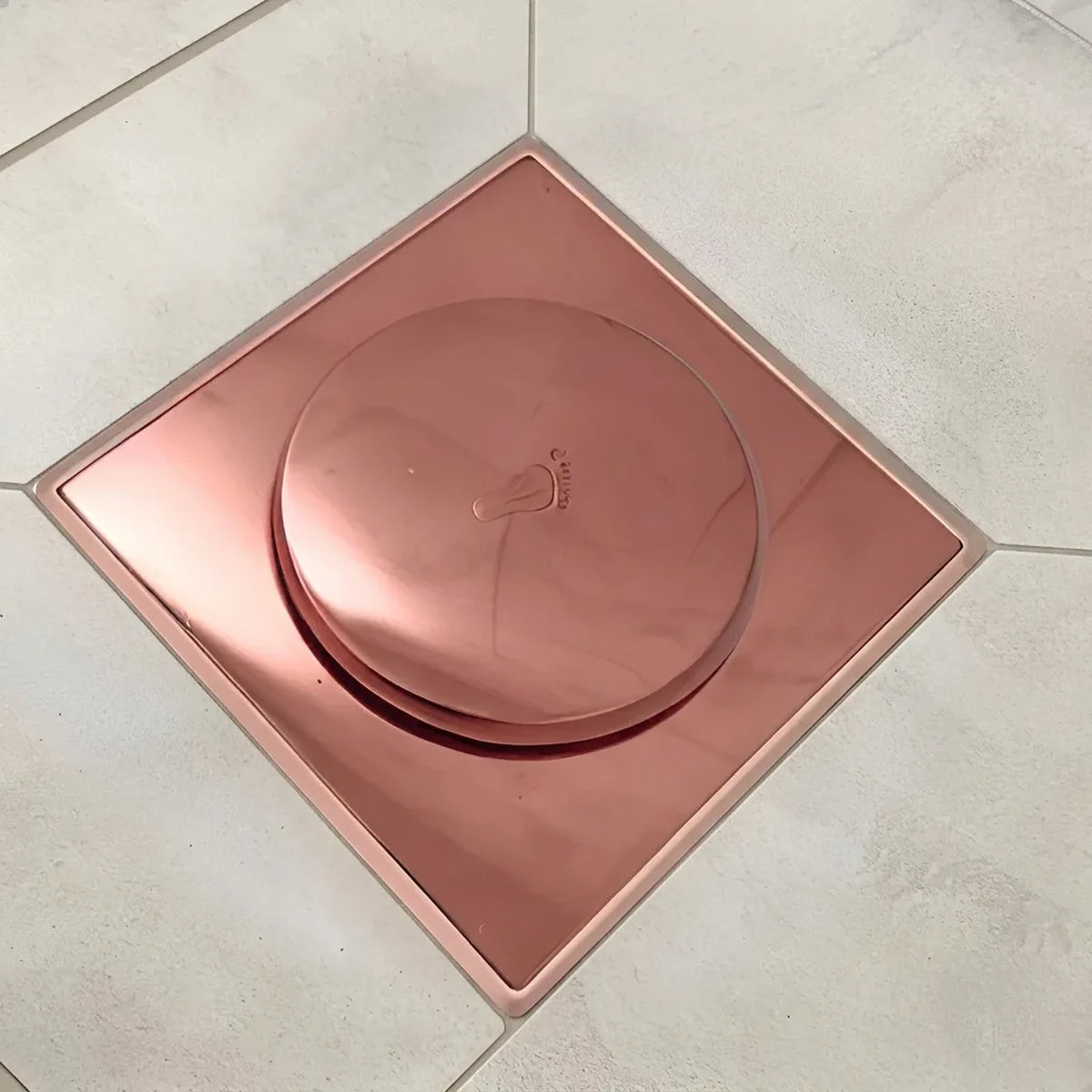 Ralo click inteligente 10x10 cm rose gold instalado em piso de porcelanato claro, com tampa redonda