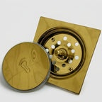 Ralo click inteligente quadrado dourado com a tampa removida, mostrando o sistema click e o cesto interno com furos de drenagem