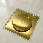 Ralo click inteligente quadrado dourado instalado em piso de porcelanato, com tampa redonda e vedacao veda cheiro