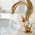 Detalhe da torneira dourada modelo cisne com água caindo do bico na cuba e manopla de cristal em primeiro plano