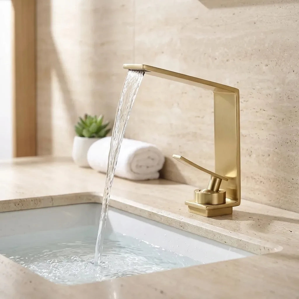 Torneira LuxStream cascata dourada instalada em bancada de travertino com cuba de embutir branca